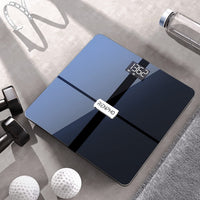 A digital Elis Aspire Smart Body Scale with a sleek black and glass design displays "132.2 lb" on its screen. The Wi-Fi connected scale, branded "Renpho EU," is placed on a gray surface. Surrounding it are a pair of black dumbbells, two white golf balls, a clear water bottle, and a pair of glasses.