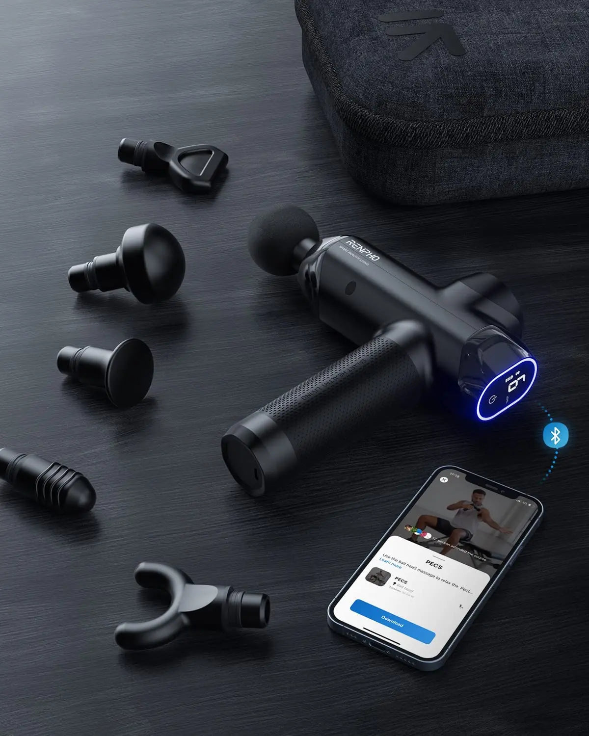 A black RENPHO Power Massage Gun with textured grip is on a dark surface surrounded by several interchangeable heads of varying shapes. A smartphone nearby displays a fitness app focused on workout recovery, and a zippered carrying case is in the background. The massage gun's controls are illuminated with blue light.