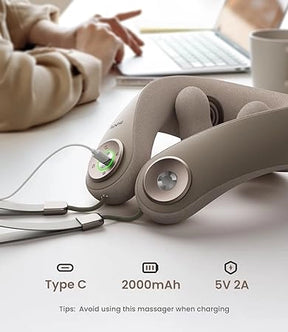 A close-up of a beige cordless massage device with a Type C charging port is shown on a table. The device indicates a 2000mAh battery and 5V 2A charging specs. In the background, a person types on a laptop next to a coffee cup. A tip on the image advises avoiding use of the Renpho EU U-Neck Mini Neck Shoulder Massager while charging.