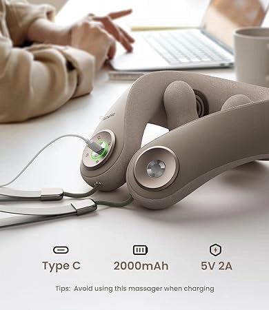 A close-up of a beige cordless massage device with a Type C charging port is shown on a table. The device indicates a 2000mAh battery and 5V 2A charging specs. In the background, a person types on a laptop next to a coffee cup. A tip on the image advises avoiding use of the Renpho EU U-Neck Mini Neck Shoulder Massager while charging.